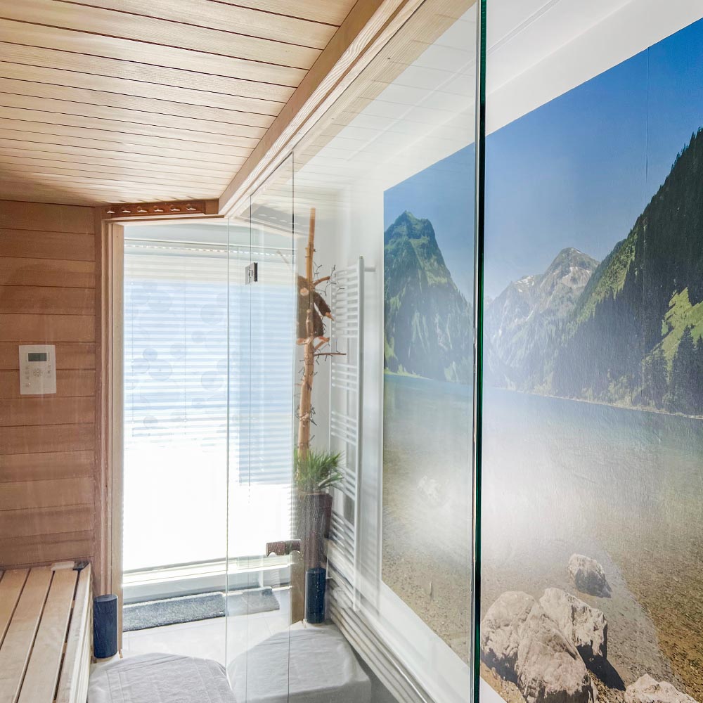 Sauna mit Glasfront im Badezimmer und Blick auf eine Fototapete mit Bergen